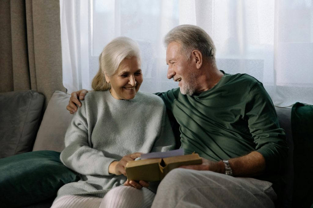 Adultos mayores sentados en un sofá leyendo y sonriendo. Pañales para adultos calzón desechable para adulto